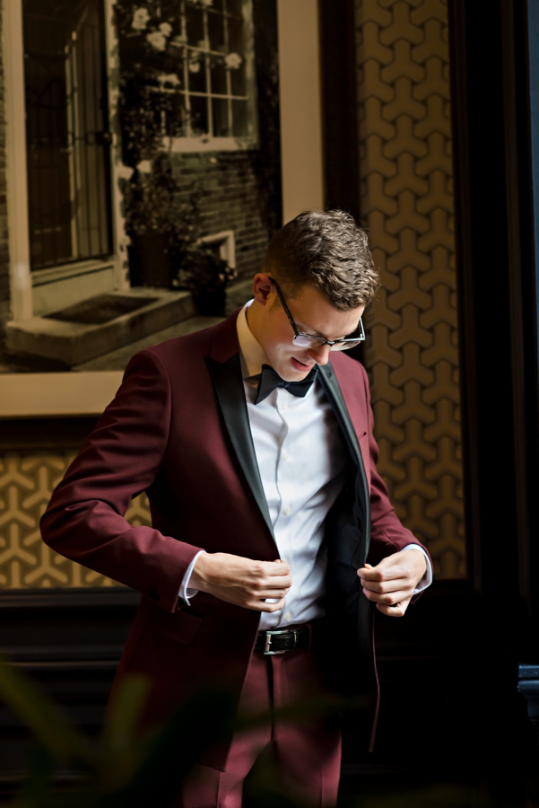 A groom buttoning up his maroon suit before the ceremony.